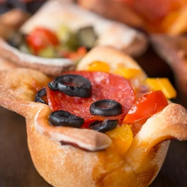 Close-up of a freshly baked mini pizza with pepperoni, olives, and bell pepper toppings