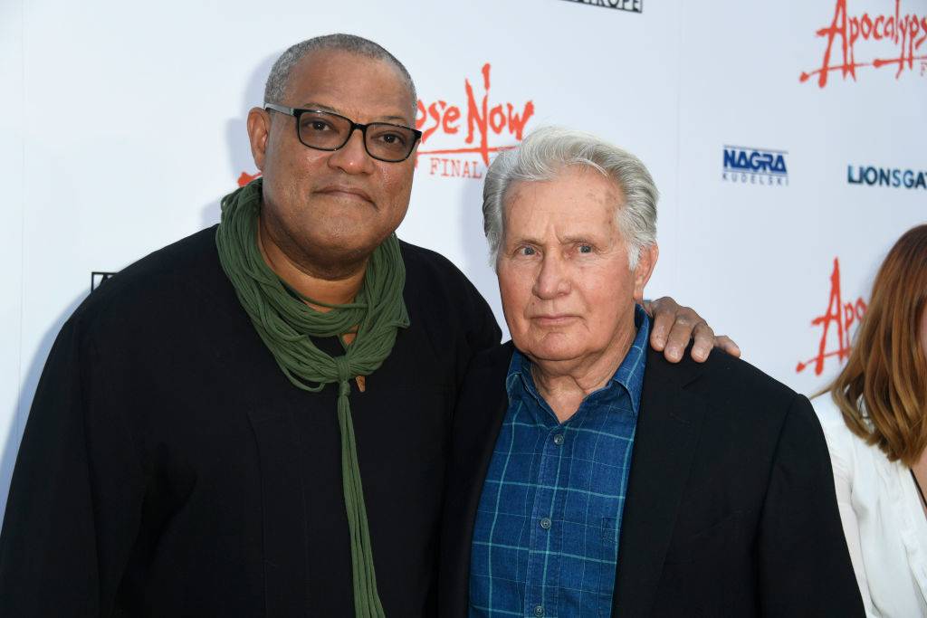 Two men standing together, one wearing glasses and a scarf, the other in a collared shirt and jacket