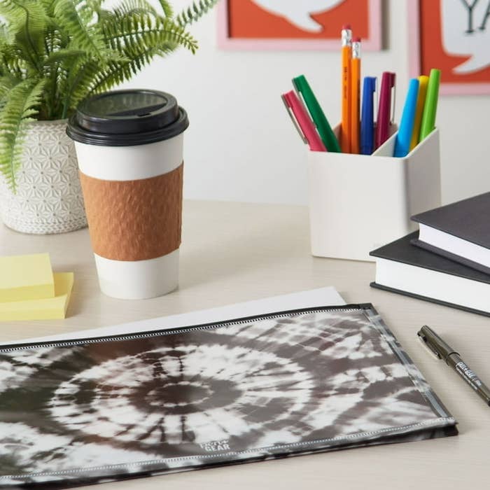 A tie-dye patterned planner rests on a desk beside a coffee cup and a holder with pens