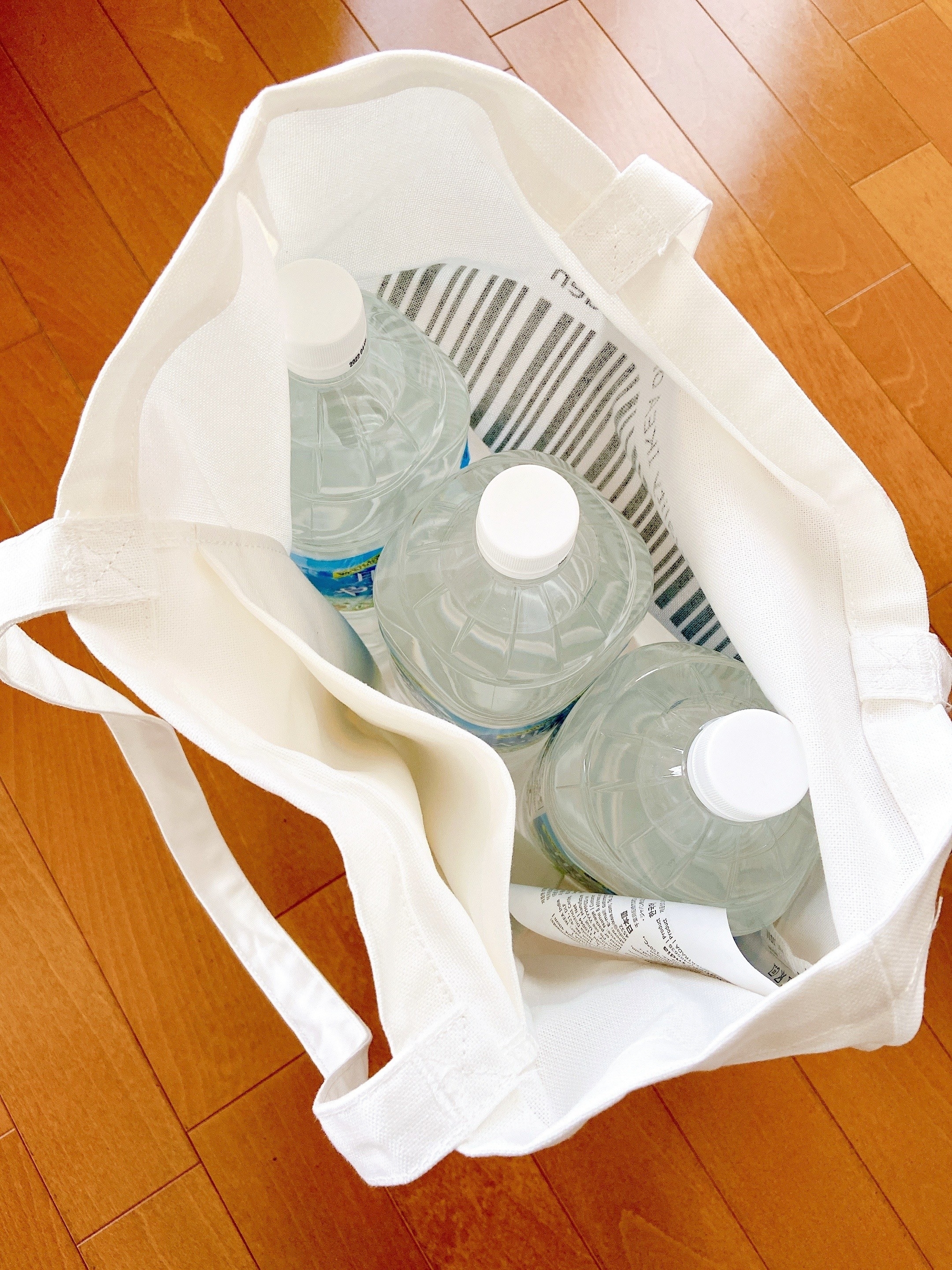白いショッピングバッグの中に、3本のペットボトルの水が入っています。