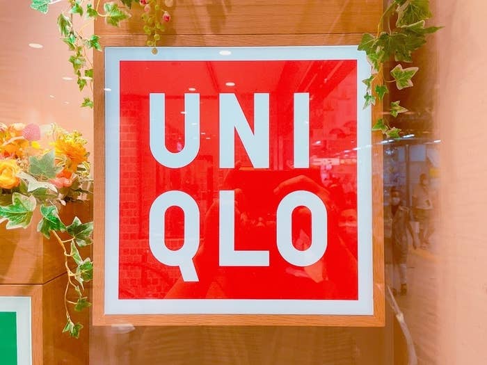 Sign of UNIQLO brand on a store window, surrounded by decorative greenery