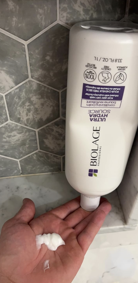 Hand dispensing shampoo from a mounted Biolage bottle