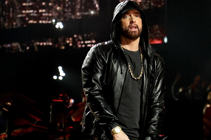 Eminem performing on stage in a leather jacket and baseball cap