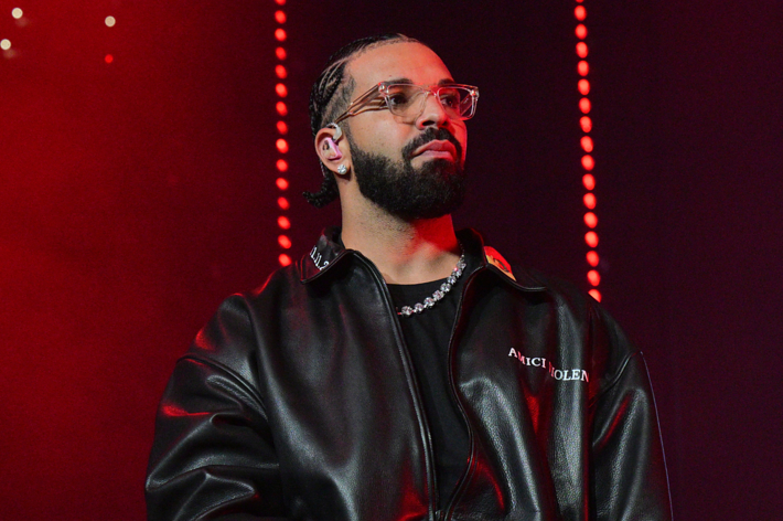 Drake in a black jacket performs on stage with red lights in the background