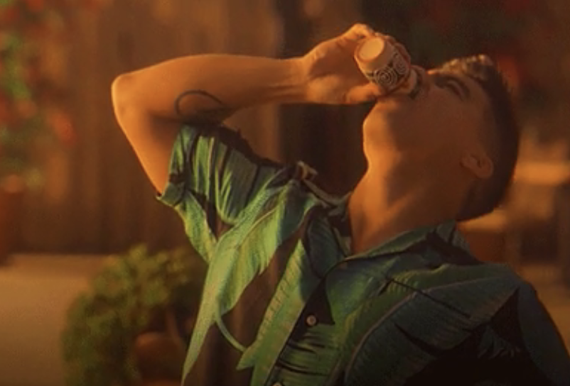 Person drinking from a bottle, wearing a casual short-sleeved shirt, in a warmly lit setting