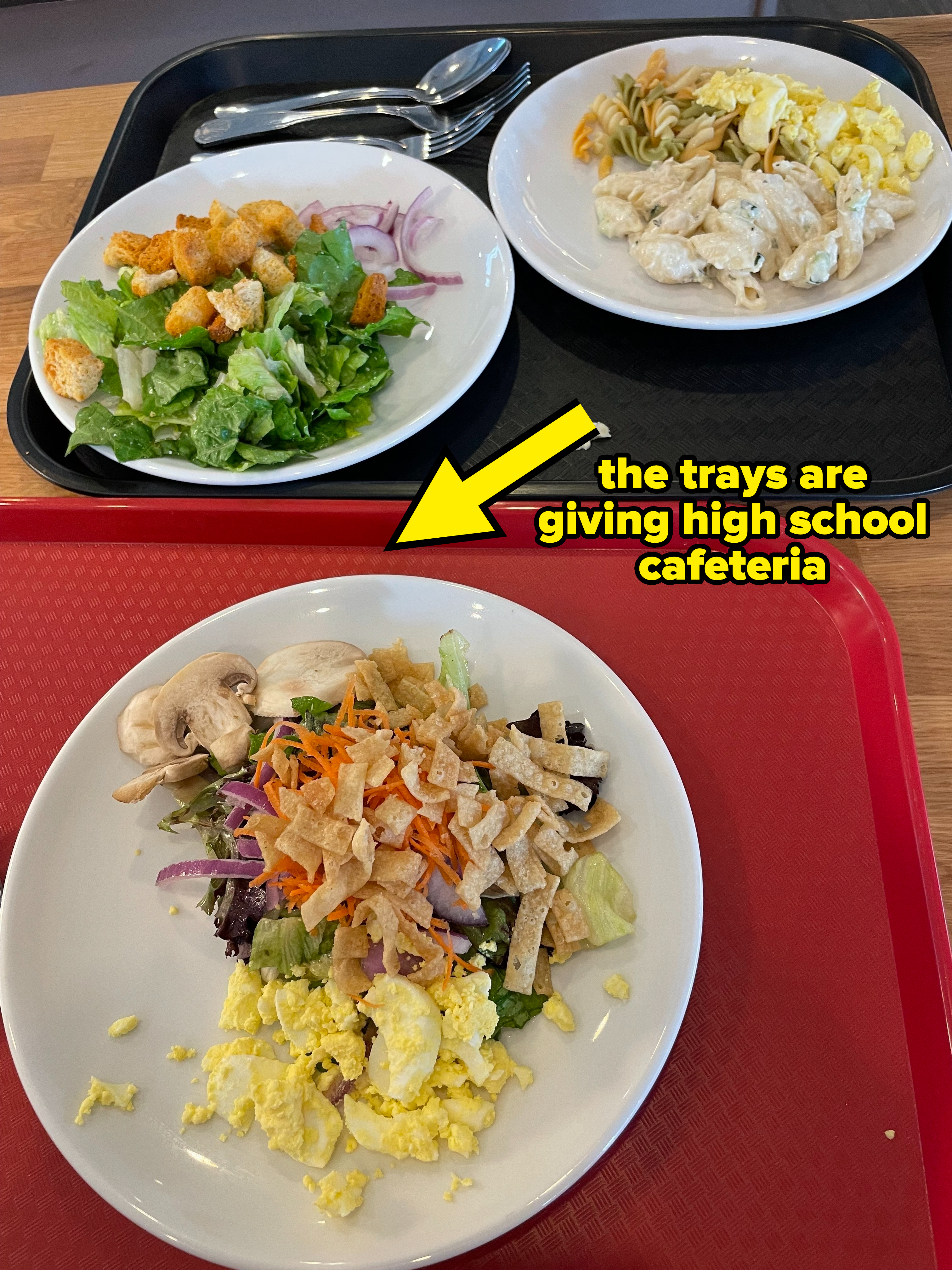 Two cafeteria trays with a salad, scrambled eggs, pasta, and mushrooms