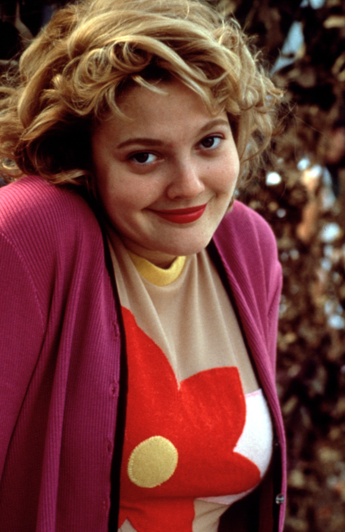 Drew Barrymore smiling, wearing a heart-patterned top and a cardigan