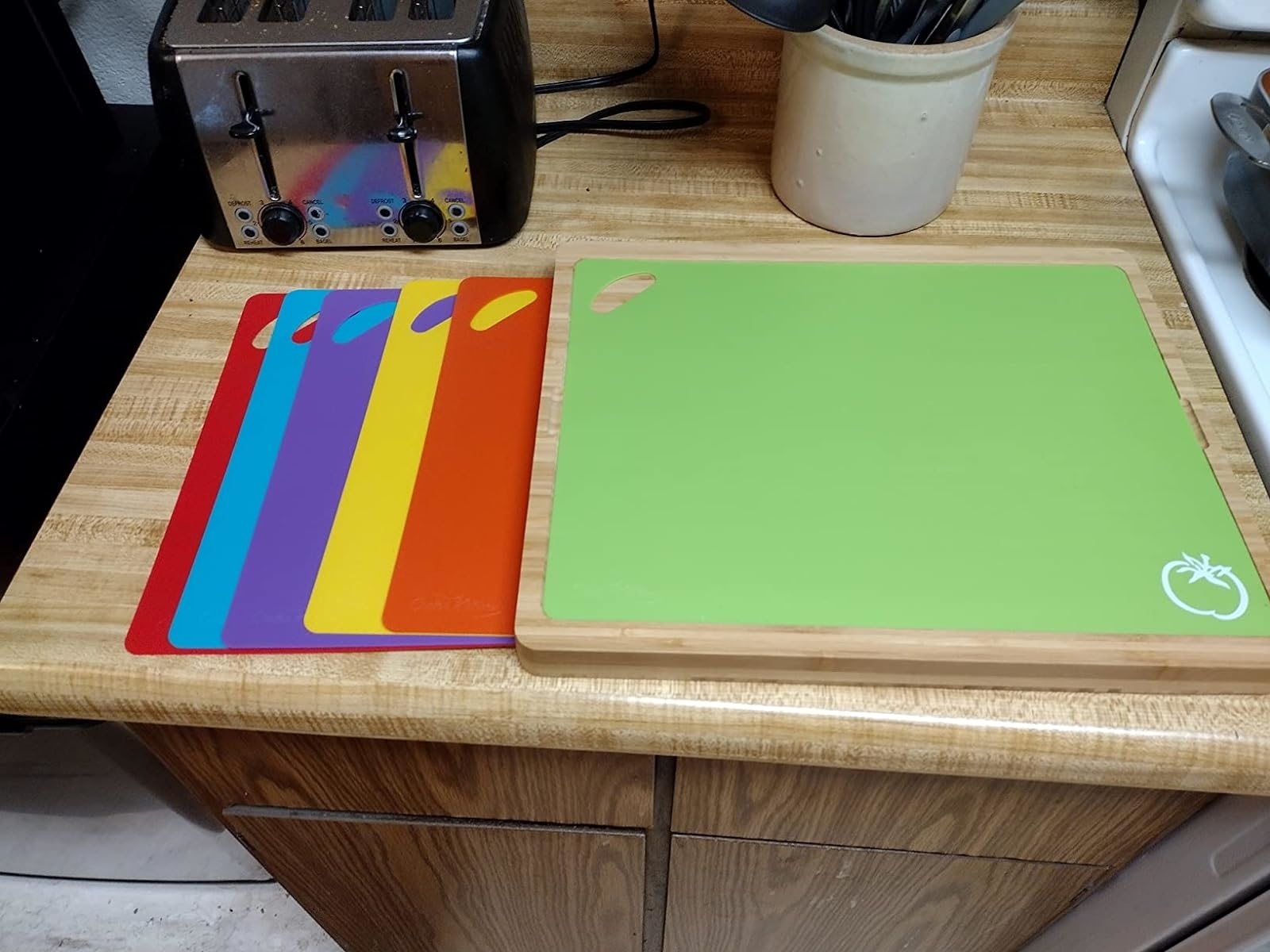 A set of multicolored cutting boards on a kitchen counter next to a green cutting mat with an apple logo