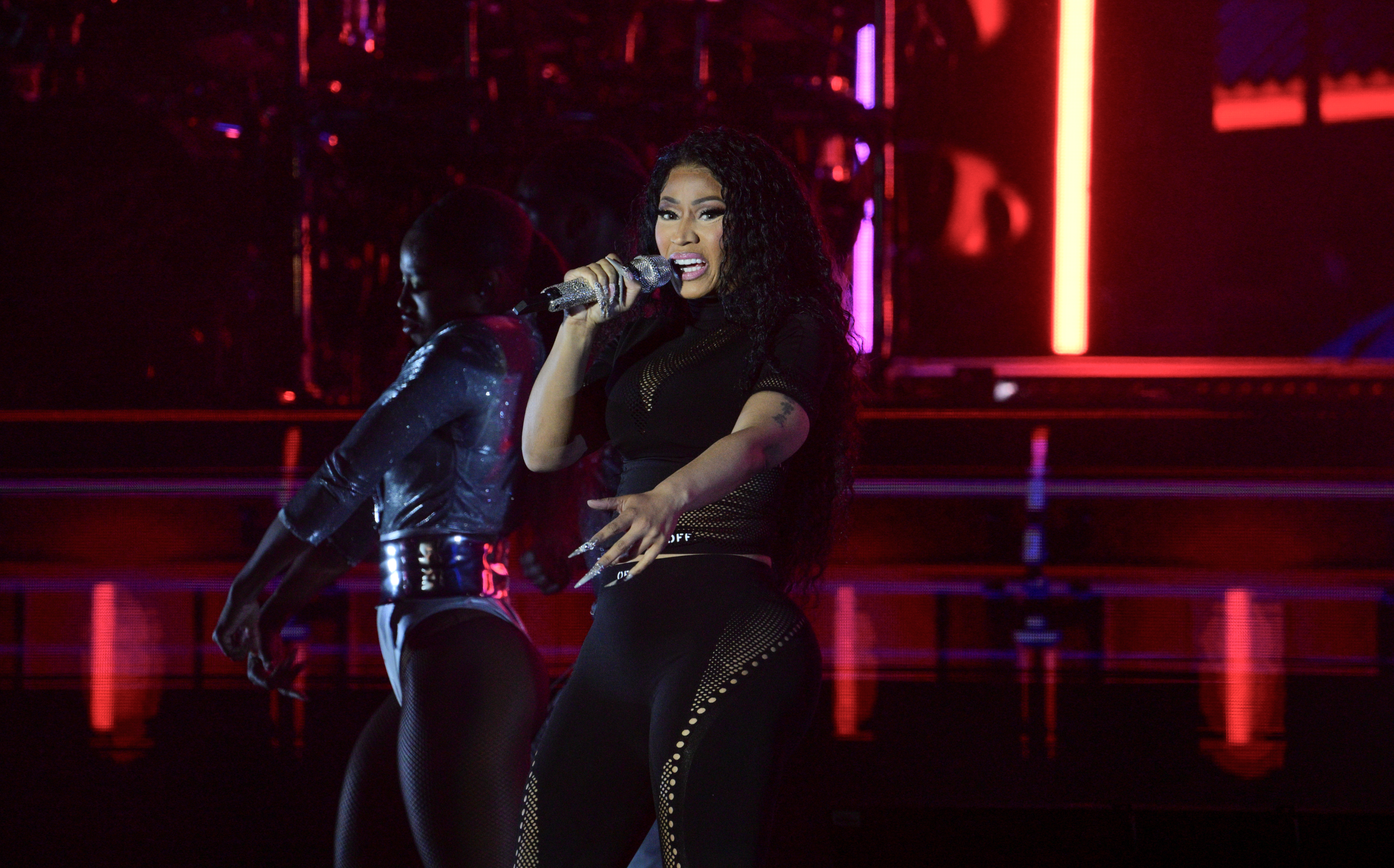 Nicki Minaj performs on stage in a black outfit with a dancer behind her