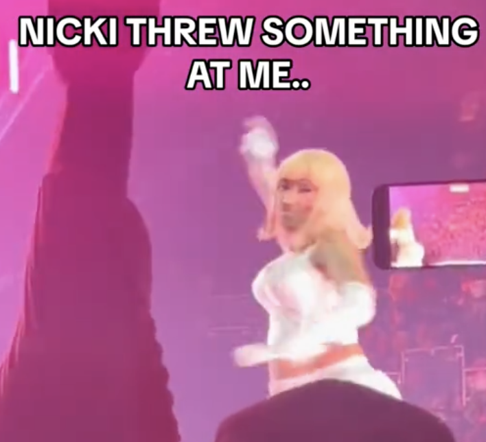 Nicki Minaj on stage throwing an object, audience in foreground, text overlay: &quot;NICKI THREW SOMETHING AT ME..&quot;