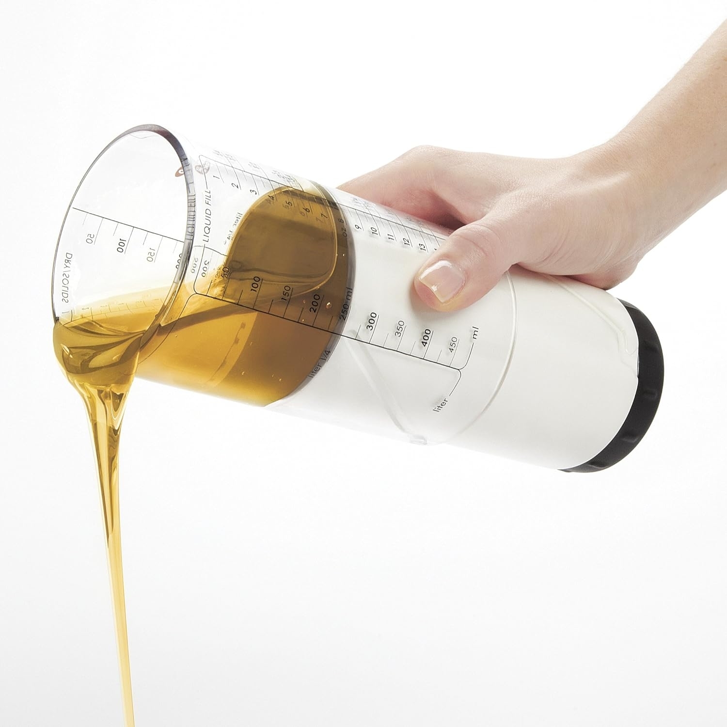 Hand pouring honey from a clear, measuring dispenser against a white background