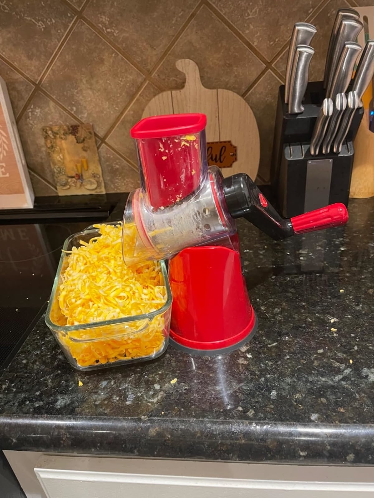 A countertop with a red cheese grater filled with shredded cheese next to a glass container