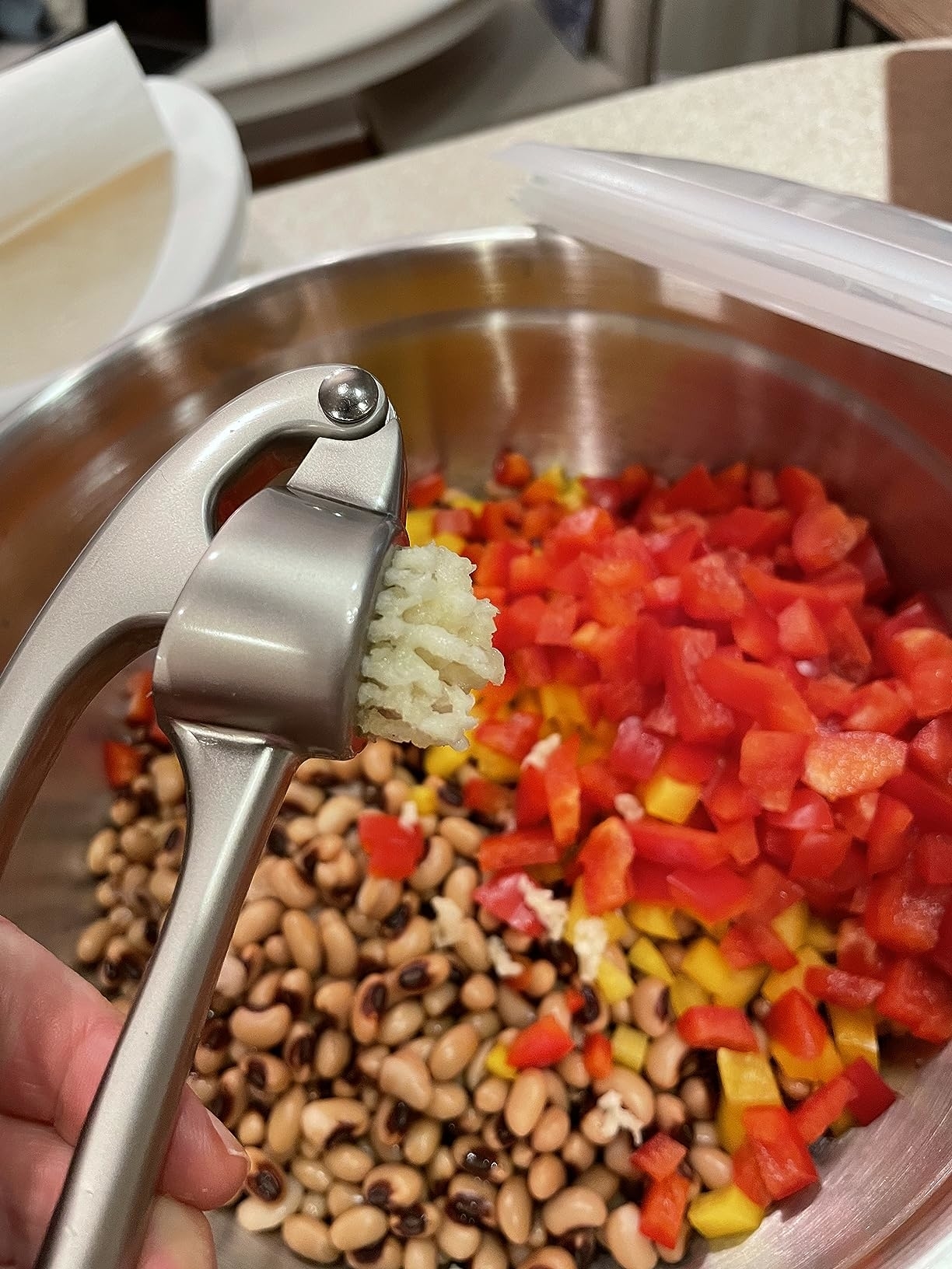 Pressed garlic over a bowl of black-eyed peas and diced bell peppers, likely for a recipe