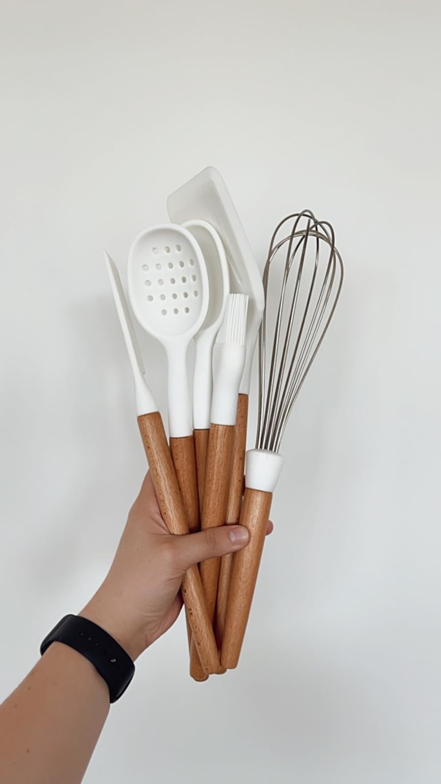 Hand holding wooden-handled kitchen utensils including a spatula, spoon, and whisk