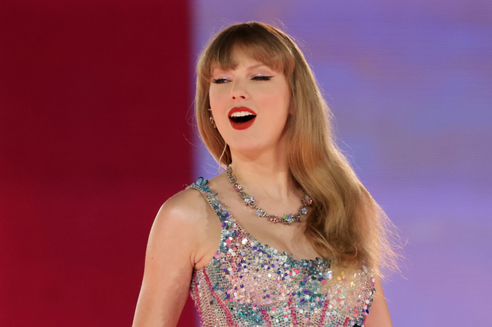 Taylor Swift is on stage singing, wearing a sparkly dress with a necklace