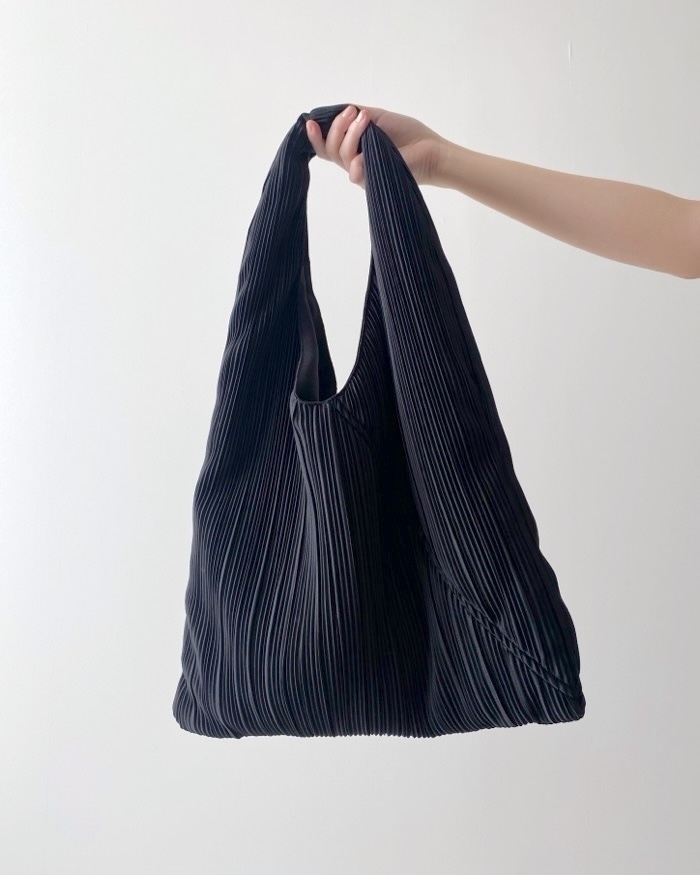 Hand holding a pleated black fabric tote bag against a plain background