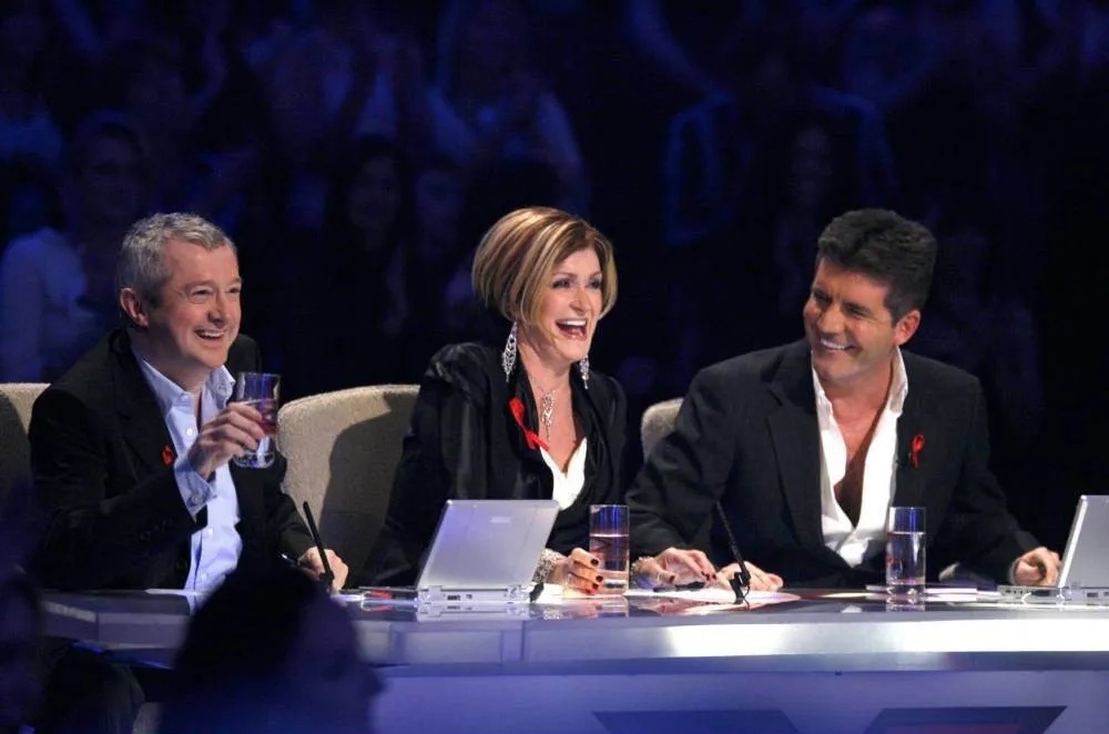 Three judges at a panel, middle judge is Sharon Osbourne, flanked by two men, all smiling and engaged