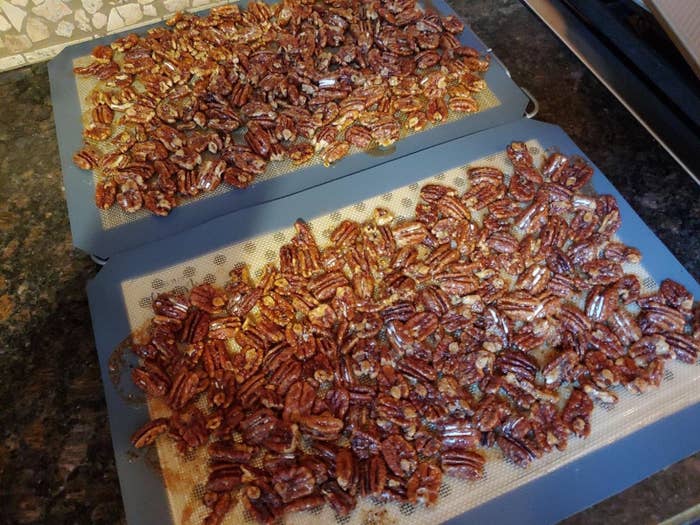 Trays with candied pecans cooling on a kitchen counter on the silicone baking mats