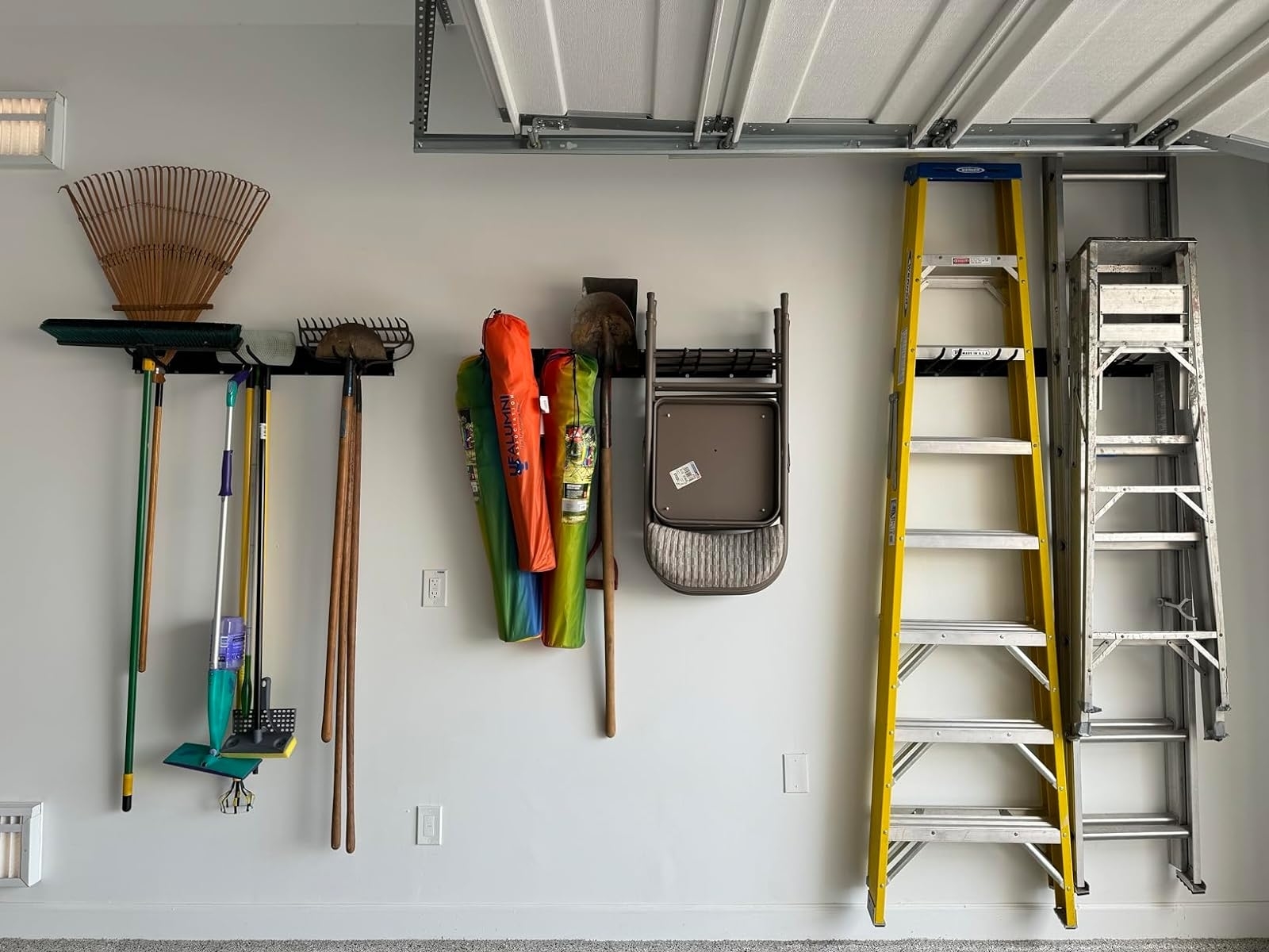 Organized garden tools and ladders hung neatly on a garage wall with the storage rack