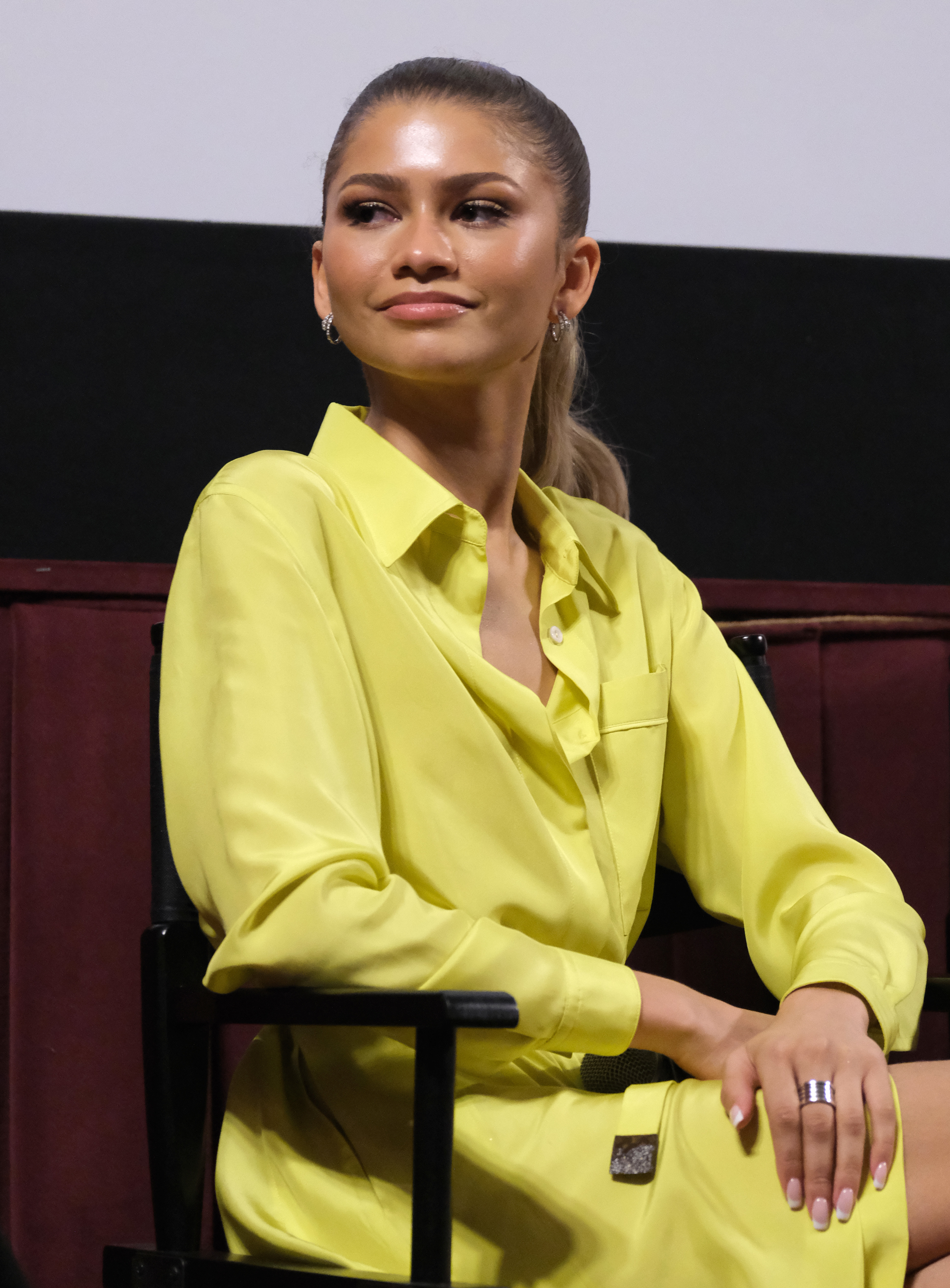 Zendaya in a bright yellow suit sits on a panel, looking to the side, with a slight smile