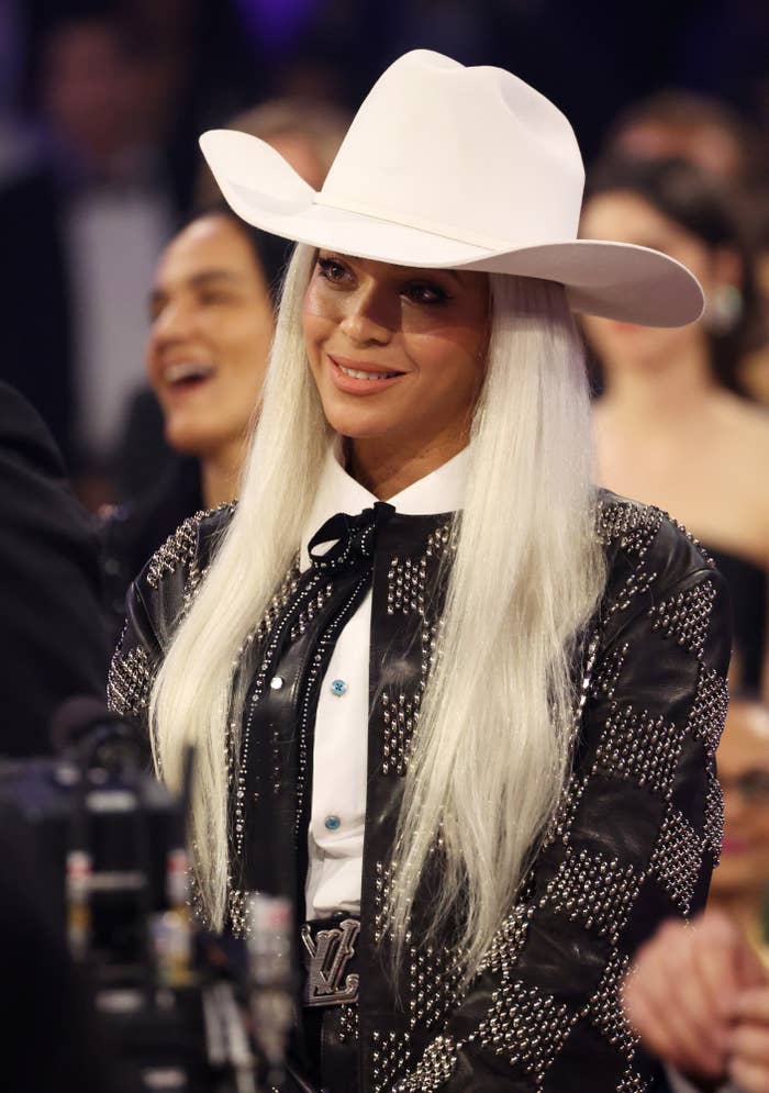 A closeup of Beyoncé at an awards show wearing a large cowboy hat and long platinum blonde hair