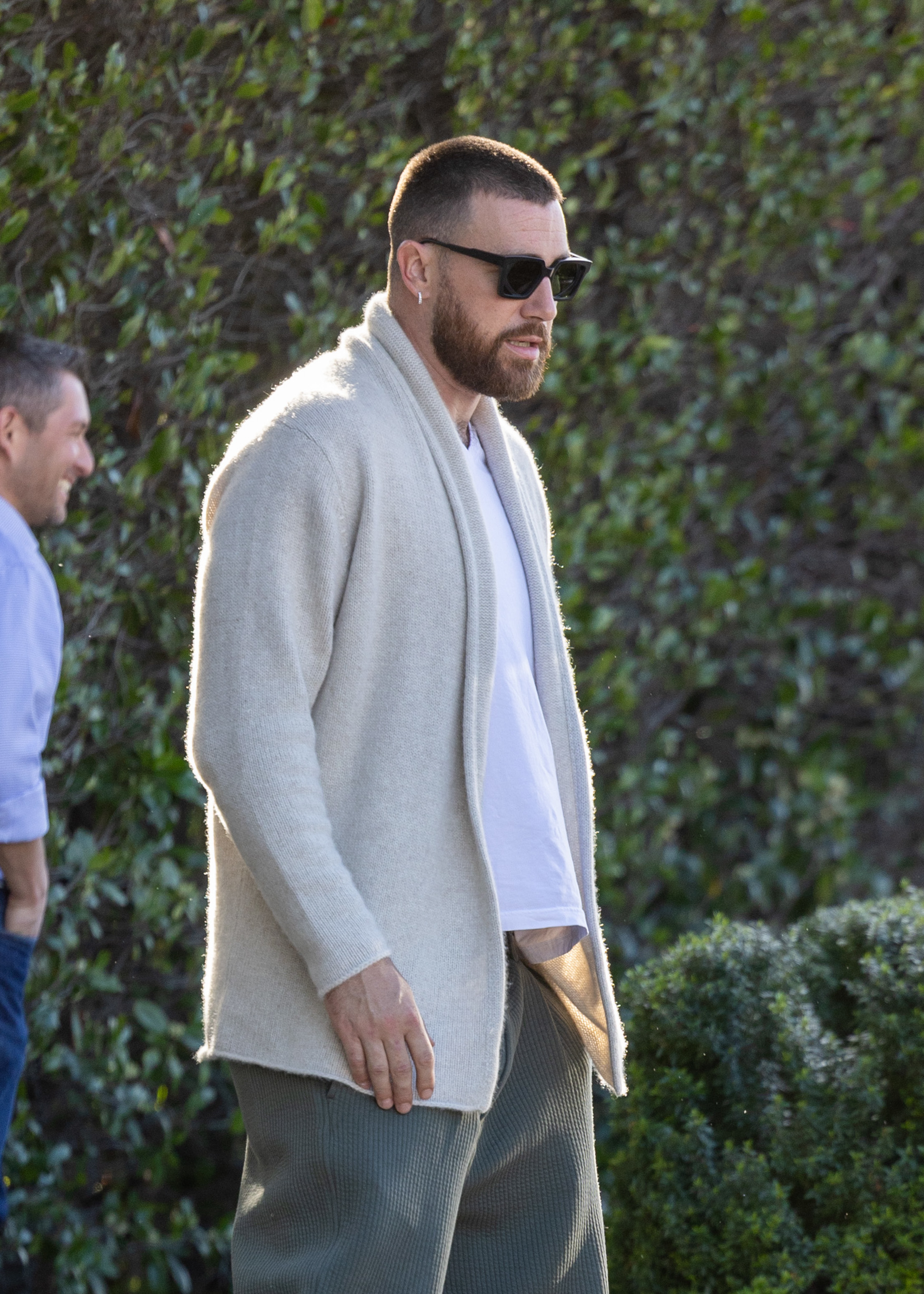 Travis Kelce in a jacket over a shirt with textured pants, walking outside