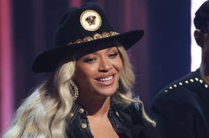 Beyoncé in a black hat and jacket with gold details, holding an award onstage
