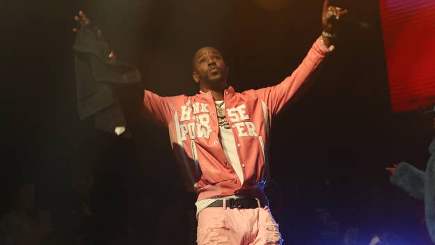 Musician on stage in a pink jacket and white pants performing with arms raised