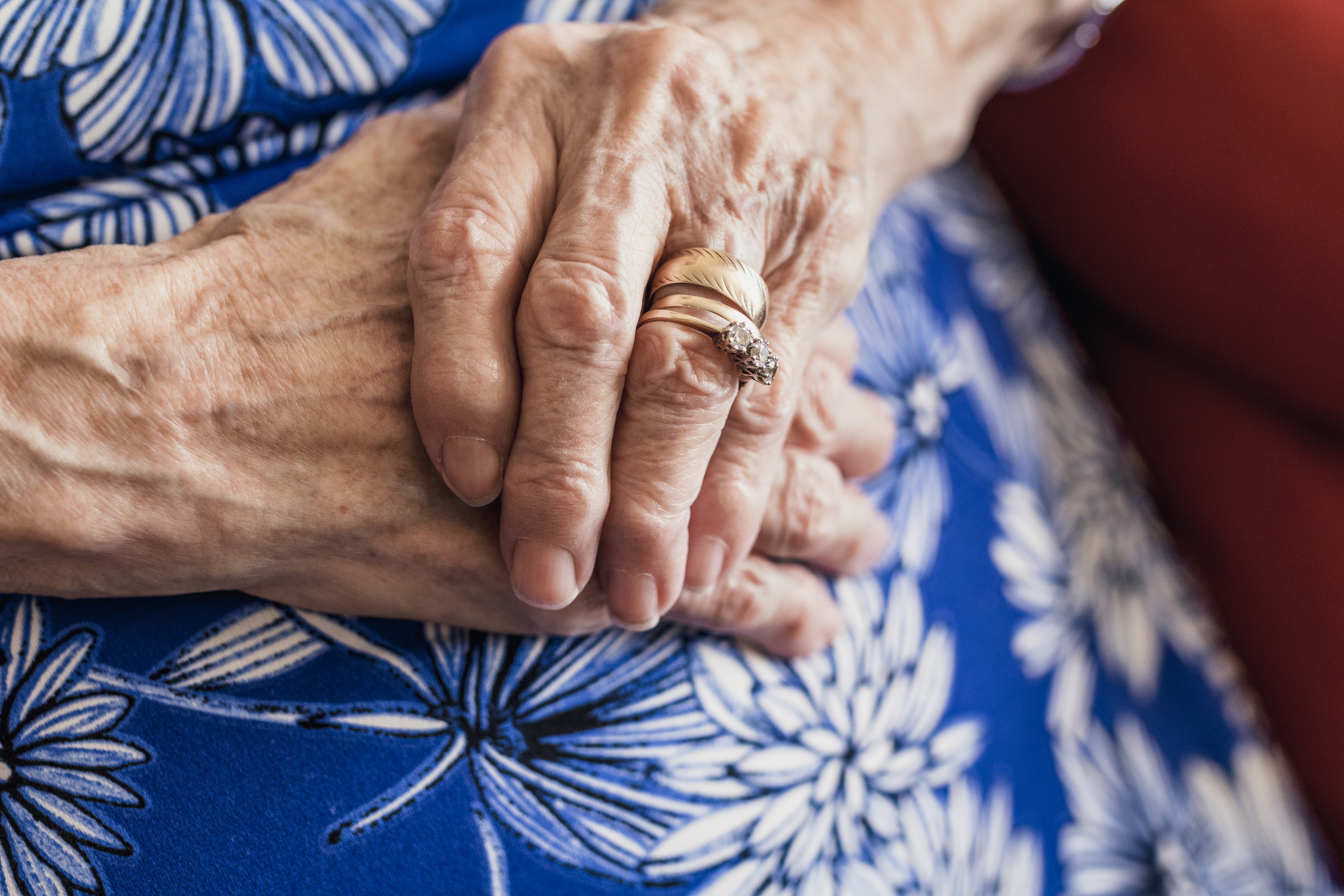 Elderly person&#x27;s hands with wedding rings resting on a floral patterned garment