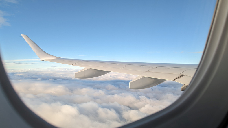 Airplane wing seen through a window, flying above the clouds