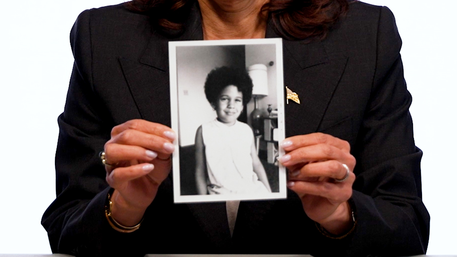 Kamala Harris holding a black and white childhood photo of herself