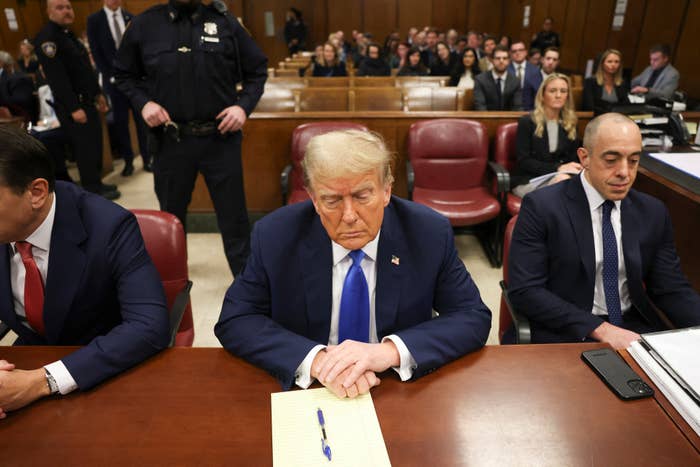 Donald Trump seated with a notepad inside a courtroom, flanked by two men