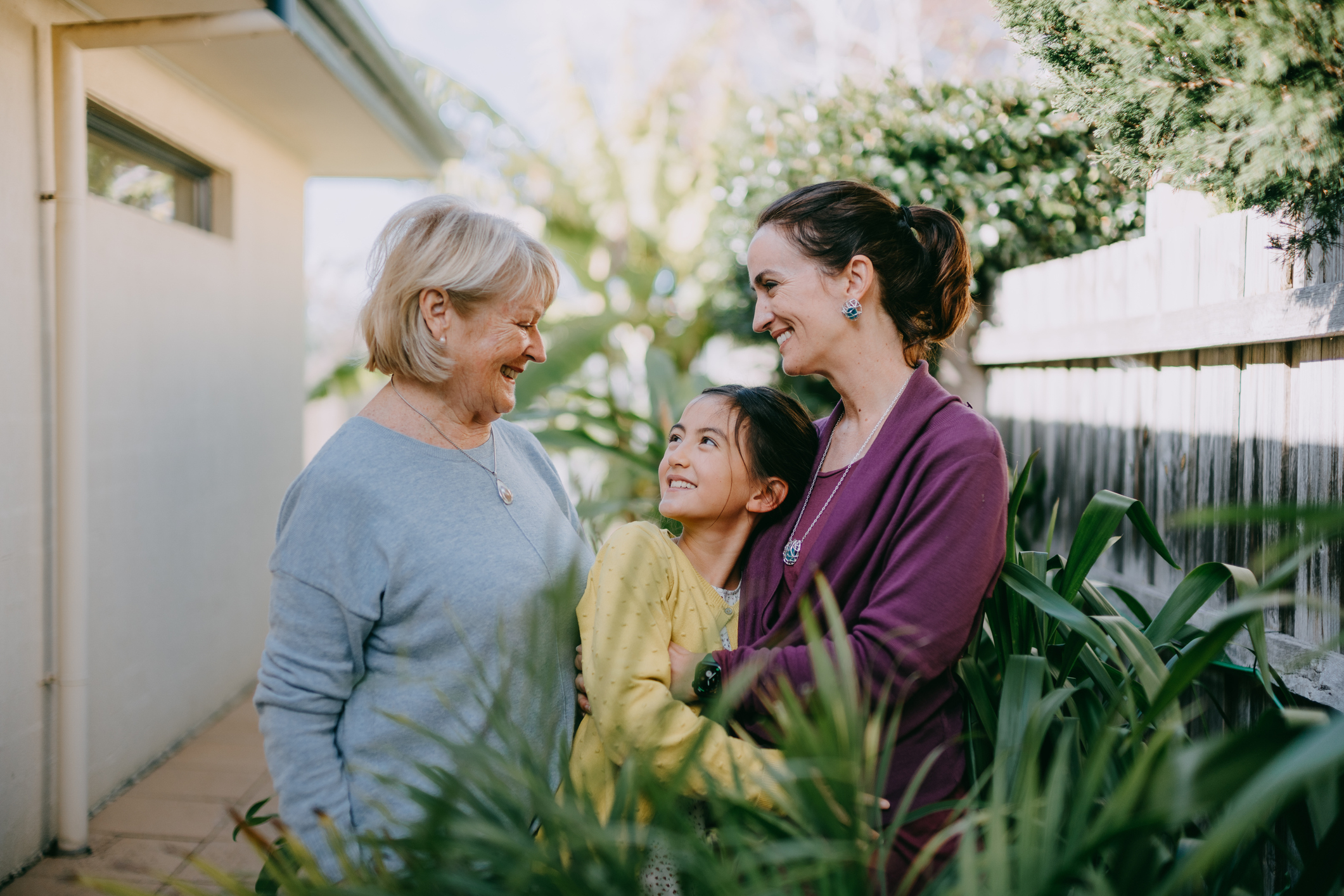 Three generations of females smiling and standing together outside near plants