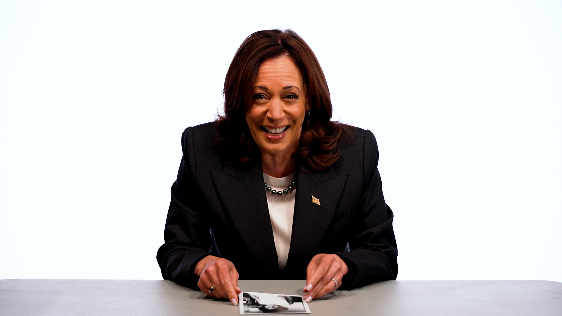 Kamala Harris sits at a table, smiling, looking at a photograph in her hands