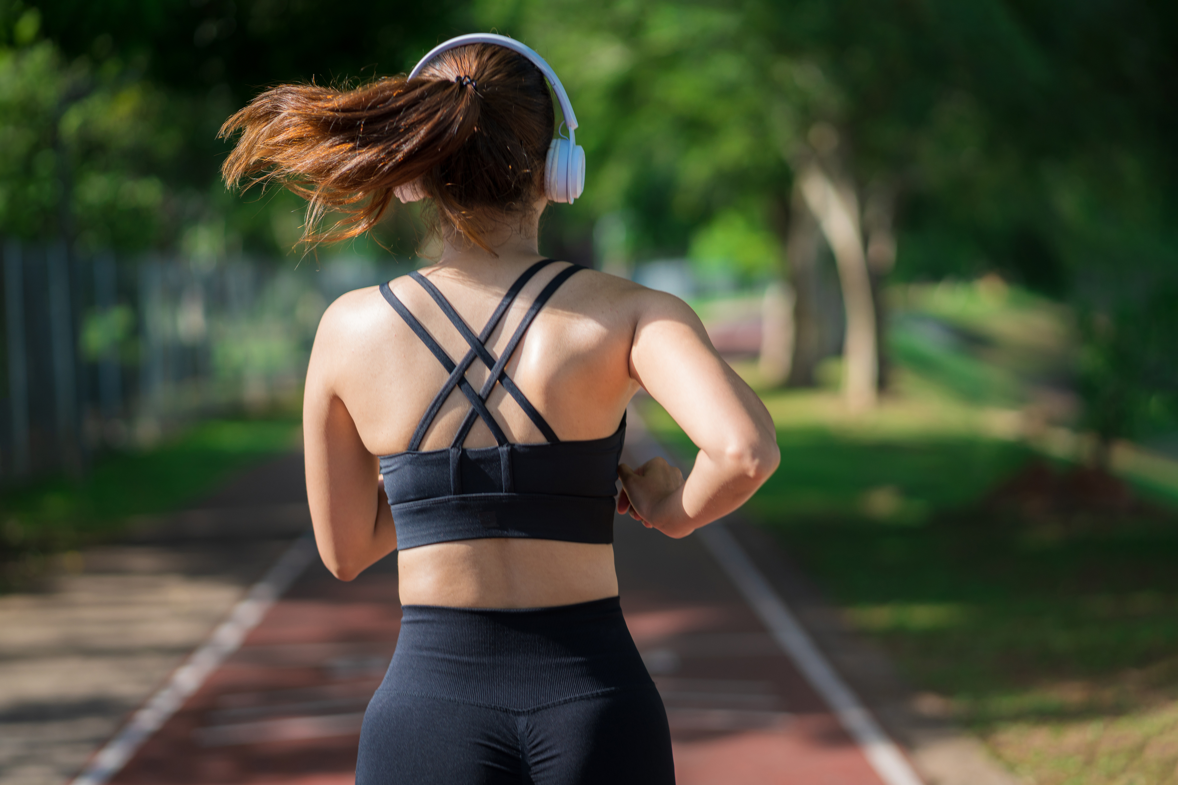 Person jogging on track in sportswear with headphones, seen from behind
