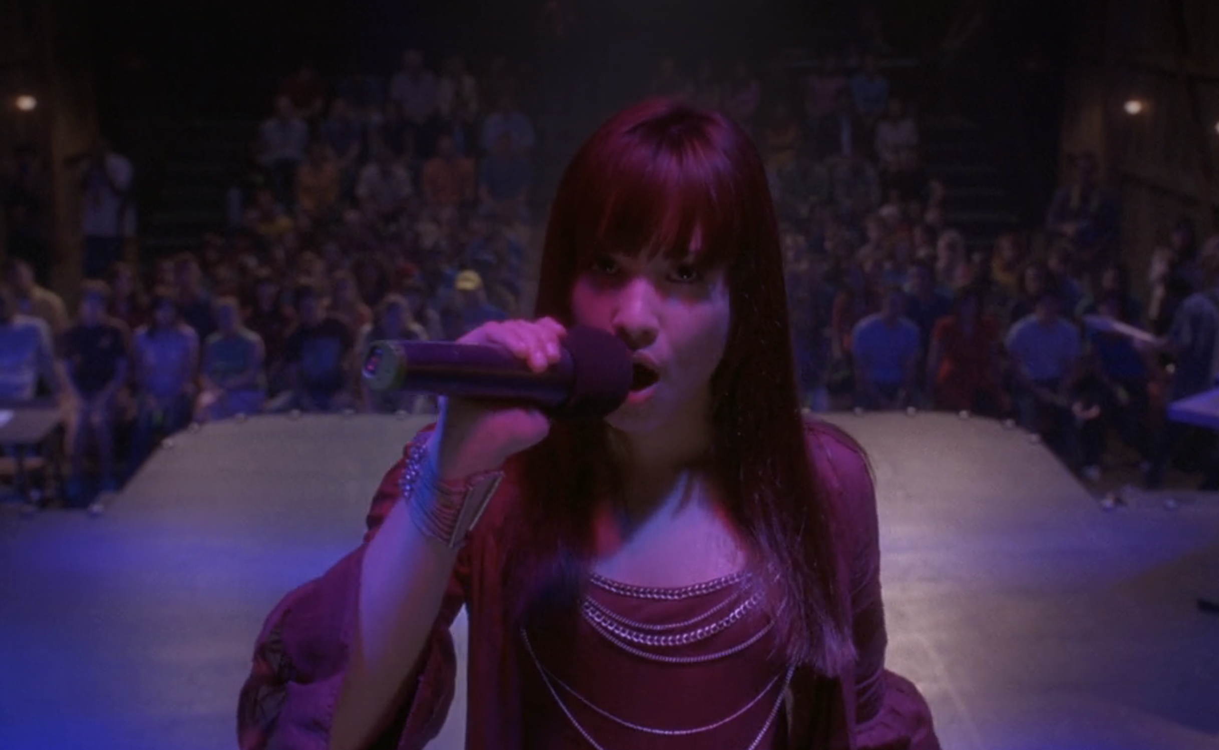 in a scene from &quot;Camp Rock,&quot; Demi singing onstage to an audience, spotlighted, wearing a casual top with microphone in hand