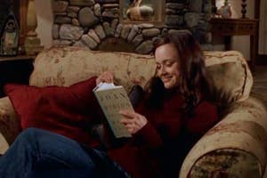 Rory Gilmore from "Gilmore Girls" reading a book on a couch in a living room.