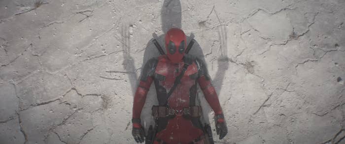 Deadpool in costume leaning against a cracked wall with arms crossed