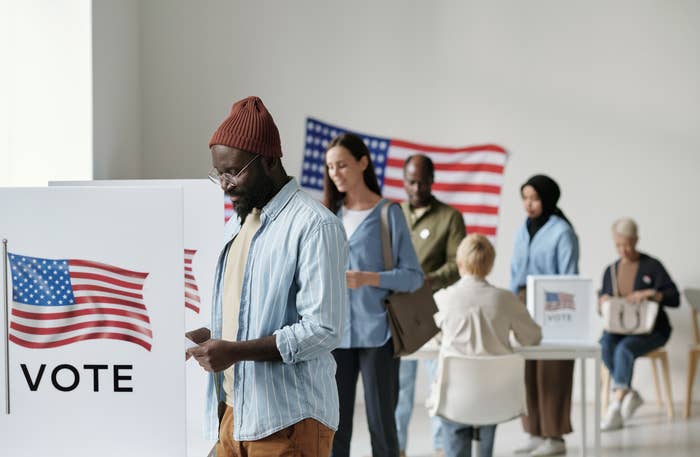 People at voting booths with &quot;VOTE&quot; signs and US flags, indicating a polling station