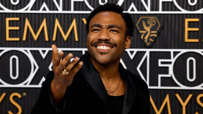 Man in a suit gestures while smiling at the Emmy Awards backdrop