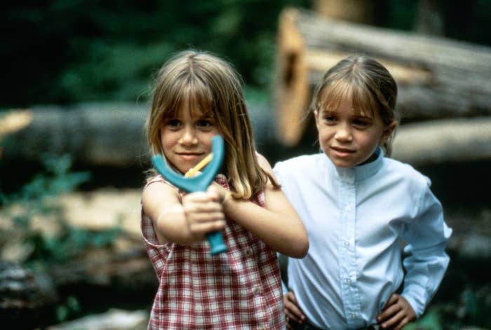 Two children outdoors, one holding a toy, standing together with trees in the background