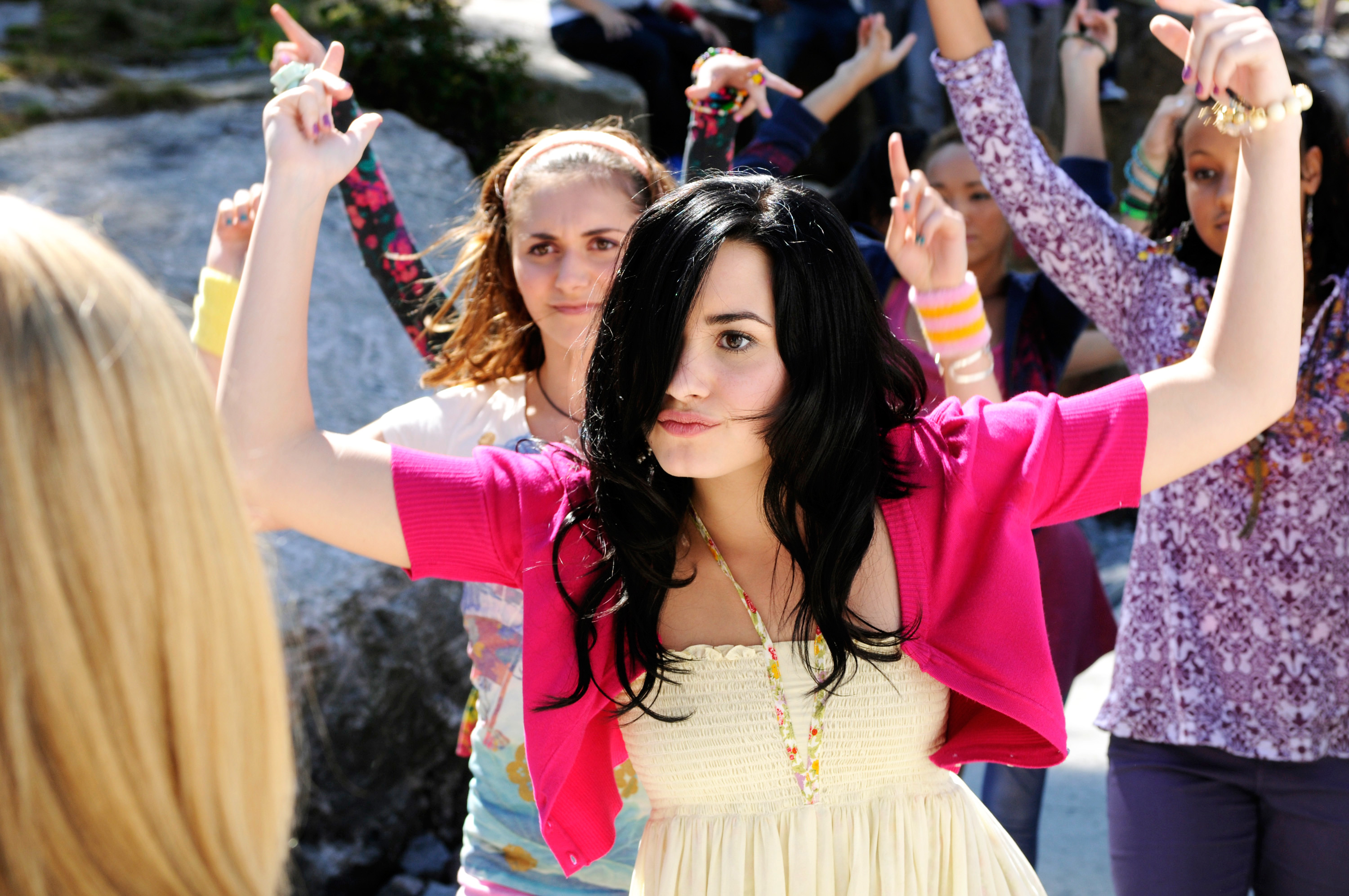 Person leading a group in dance, onlookers following the movements, outdoors in casual attire