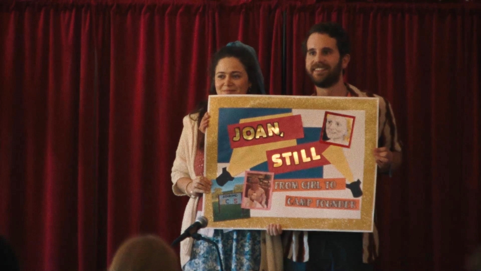 Two individuals hold a large poster with text and images for a presentation
