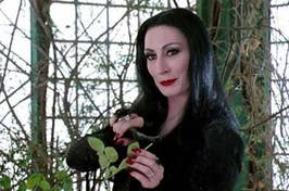 Woman styled as Morticia Addams holding a plant stem