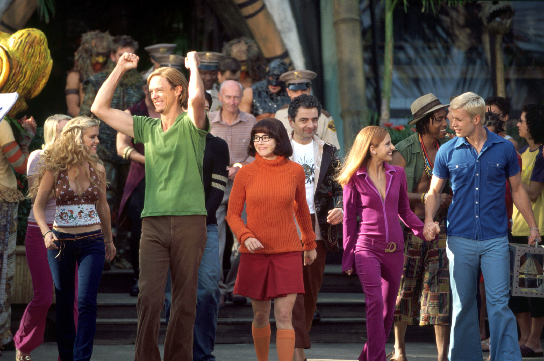 Cast of scooby doo in vintage attire walking arm-in-arm on set