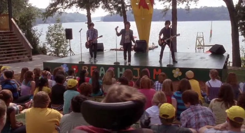 Band performs on stage at a lakeside event while audience watches