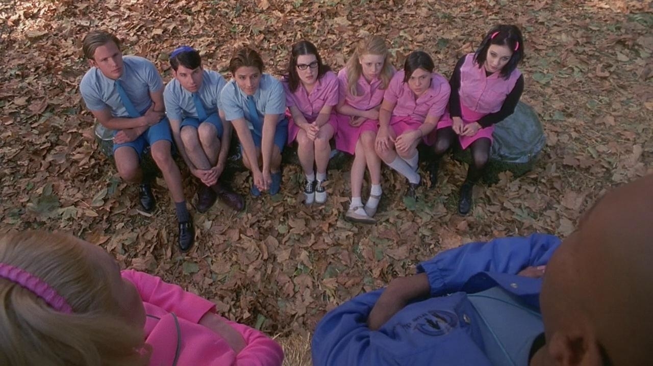 Seven individuals sitting on the ground in a circle, wearing blue and pink tops
