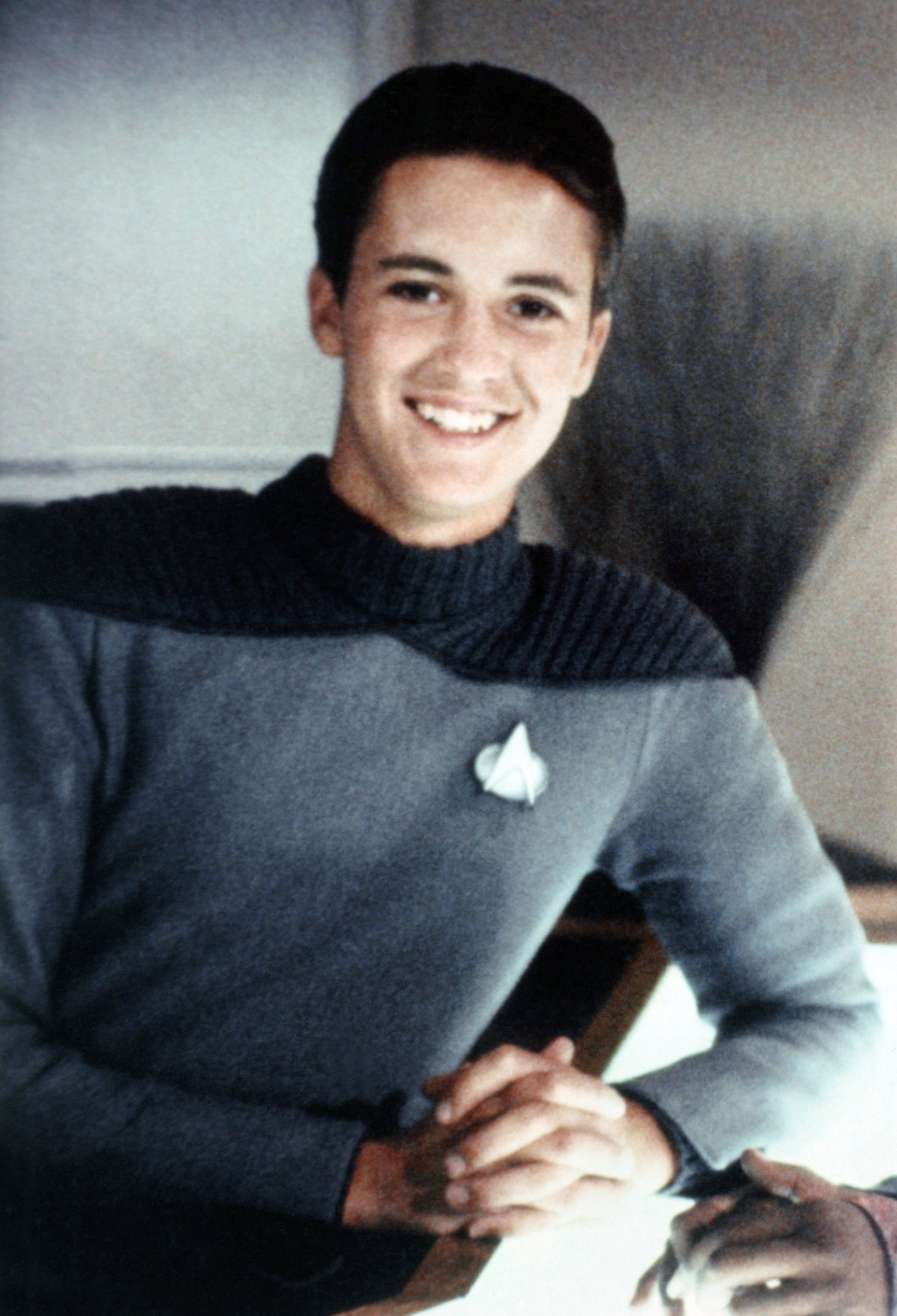 Wesley Crusher from Star Trek sitting at a table, smiling, in character attire