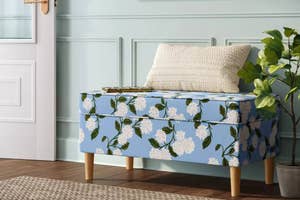 Floral upholstered storage bench with a cushion in a room, beside a plant