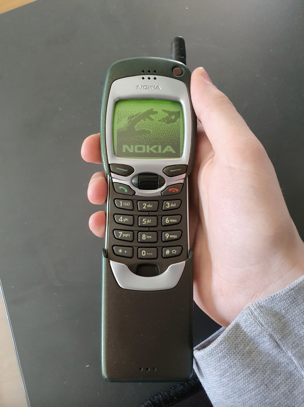 Hand holding a vintage Nokia mobile phone with physical buttons and small screen